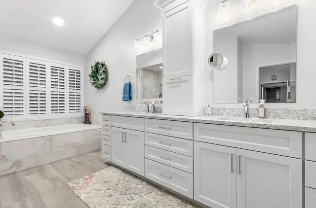 Primary bathroom with a long white double vanity, marble-look counter and a tiled tub surround