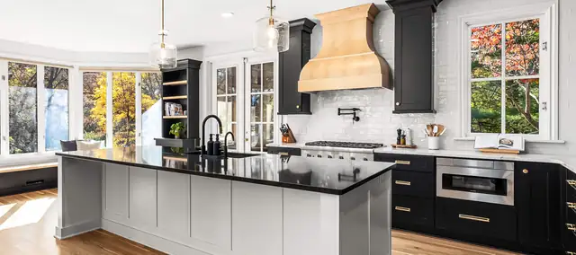 Remodeled kitchen with black lower cabinets, a natural wood range hood, white island and black countertops by MJ Kitchen & Bath