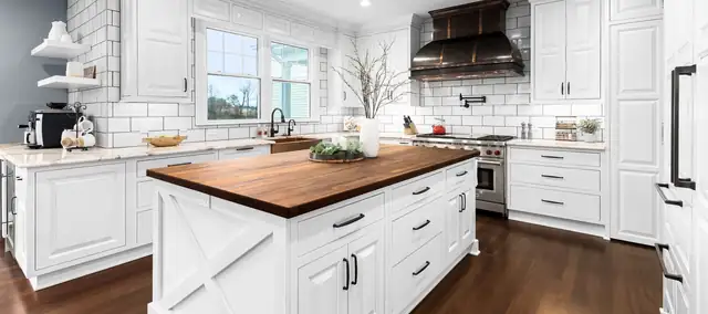 White kitchen with a butcher-block island top, X-panel island end and a black metal range hood