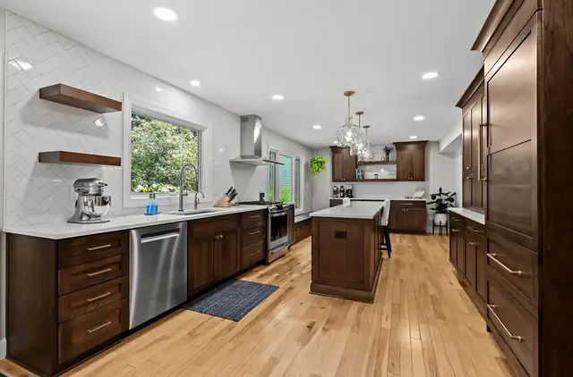 Kitchen with cherry-toned cabinets, floating wood shelves, white herringbone wall tile and a center island