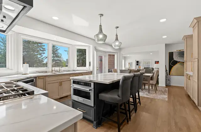 Open kitchen with light wood cabinets and a black island with stools that flows into a dining area