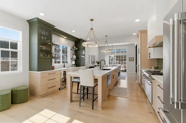 Kitchen with green glass-front cabinets, a light wood island with seating and brass pendant lights